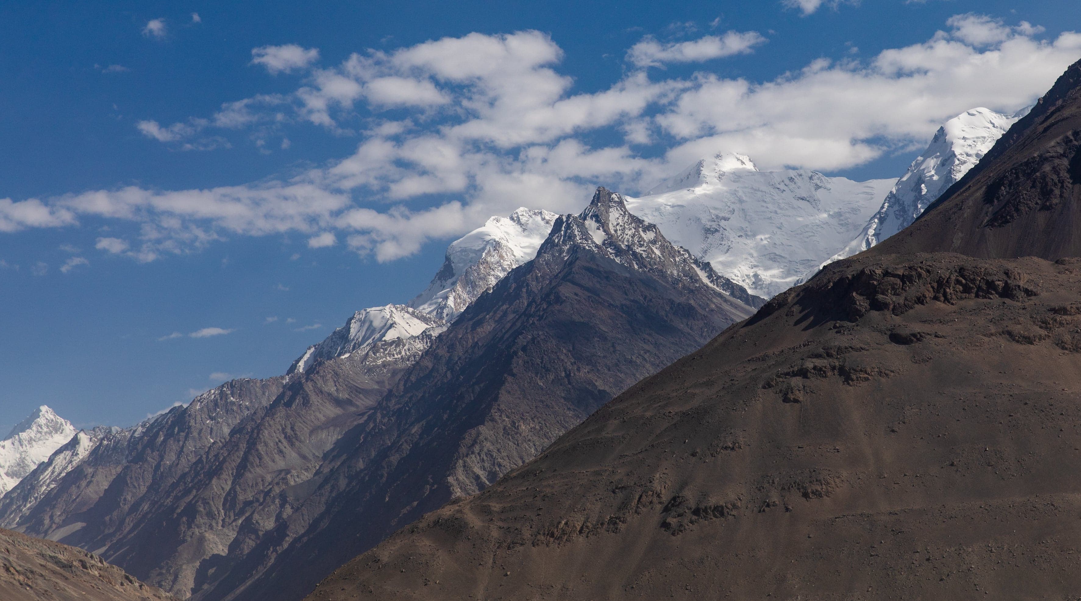 Snow-capped Hindu Kush peaks rising above a wide valley under a blue sky
