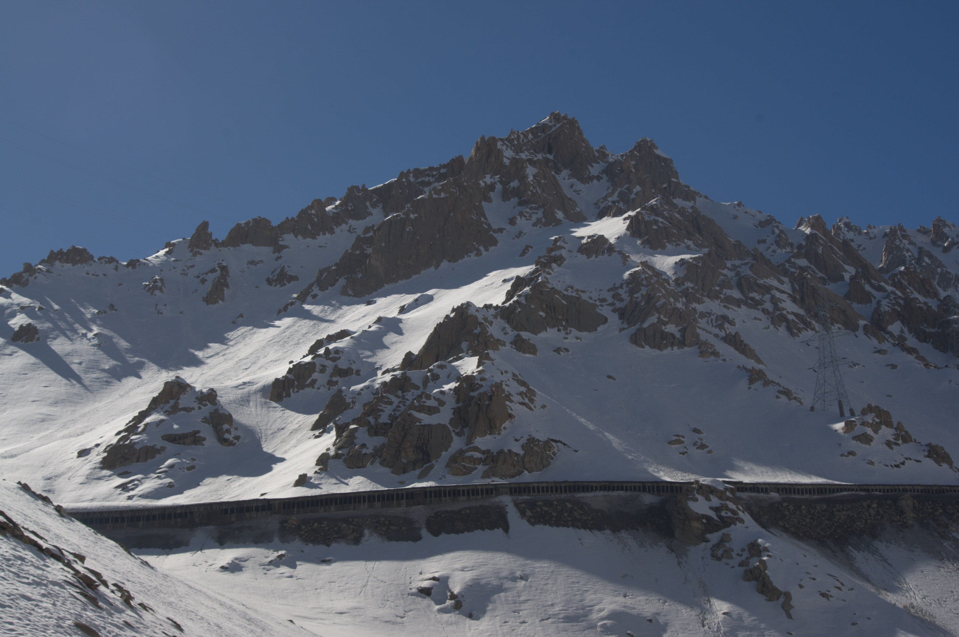 A winding mountain road crossing a snow-covered high pass in the Hindu Kush