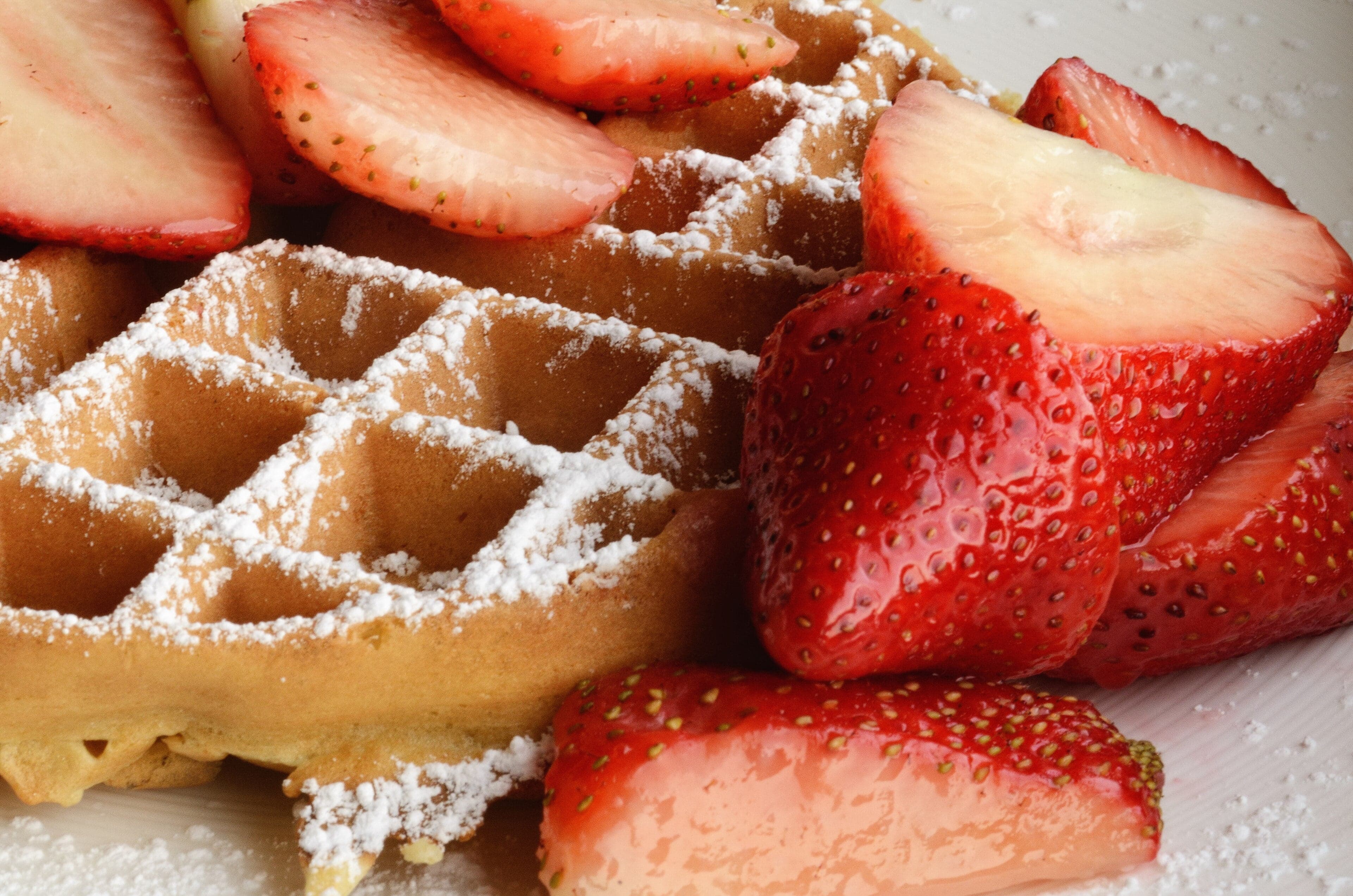 A Belgian waffle topped with strawberries and whipped cream on a paper plate