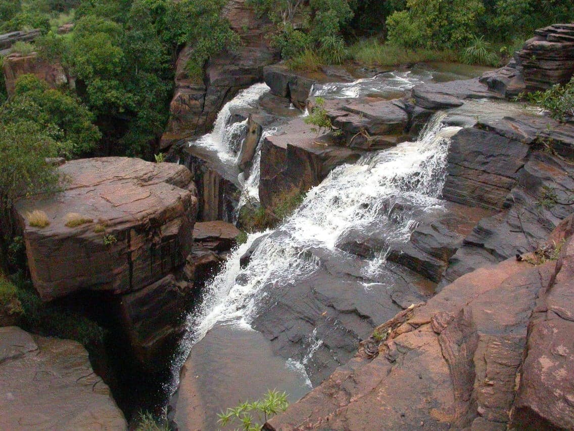 The Karfiguéla waterfalls cascading over rocks surrounded by green trees