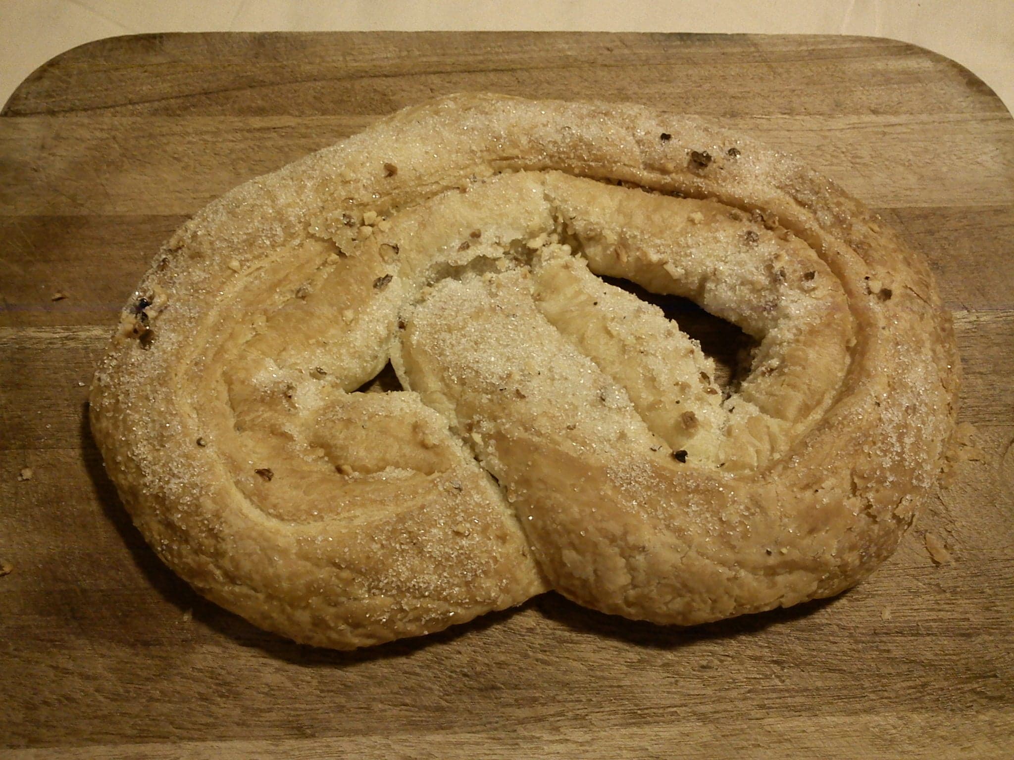 A golden braided Estonian kringle sweet bread dusted with sugar on a wooden board