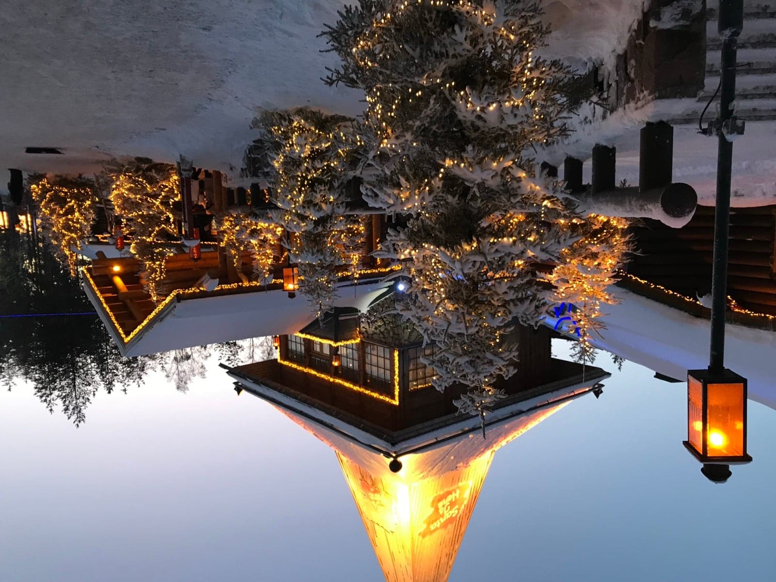 Santa Claus Village in Rovaniemi at twilight, with snow-covered fir trees lit up in fairy lights