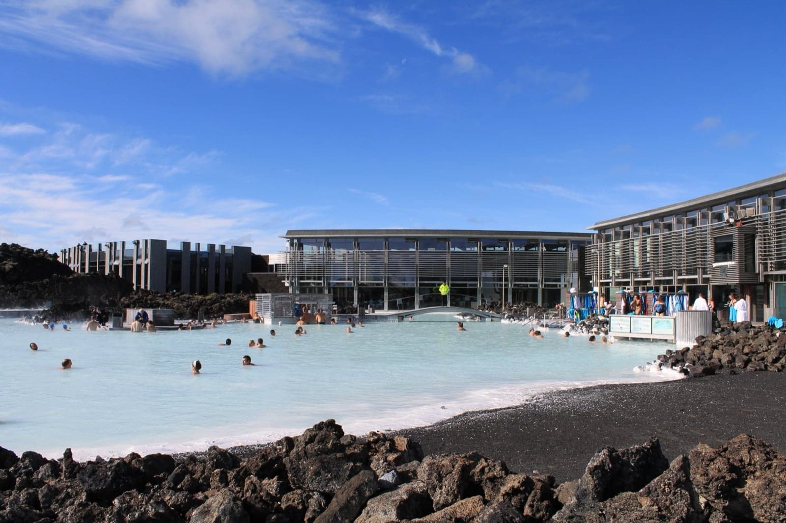The pale milky-blue water of the Blue Lagoon with black lava rocks around the edge