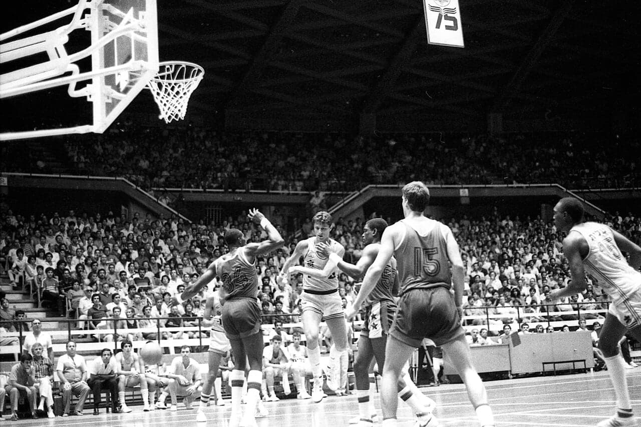 A basketball mid-flight towards a hoop in an indoor sports hall
