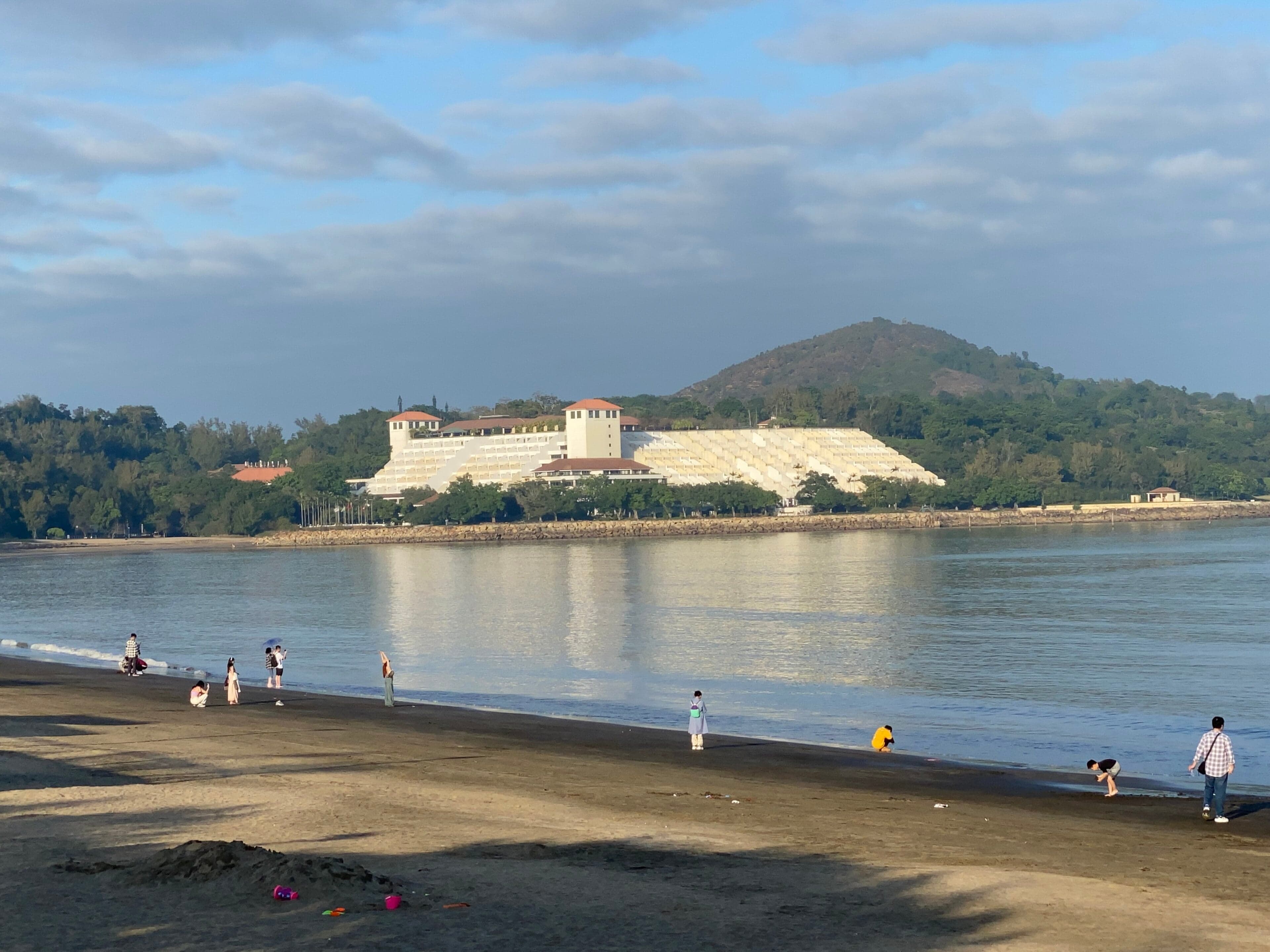 Dark volcanic sand at Hac Sa Beach in Macau with green hills behind