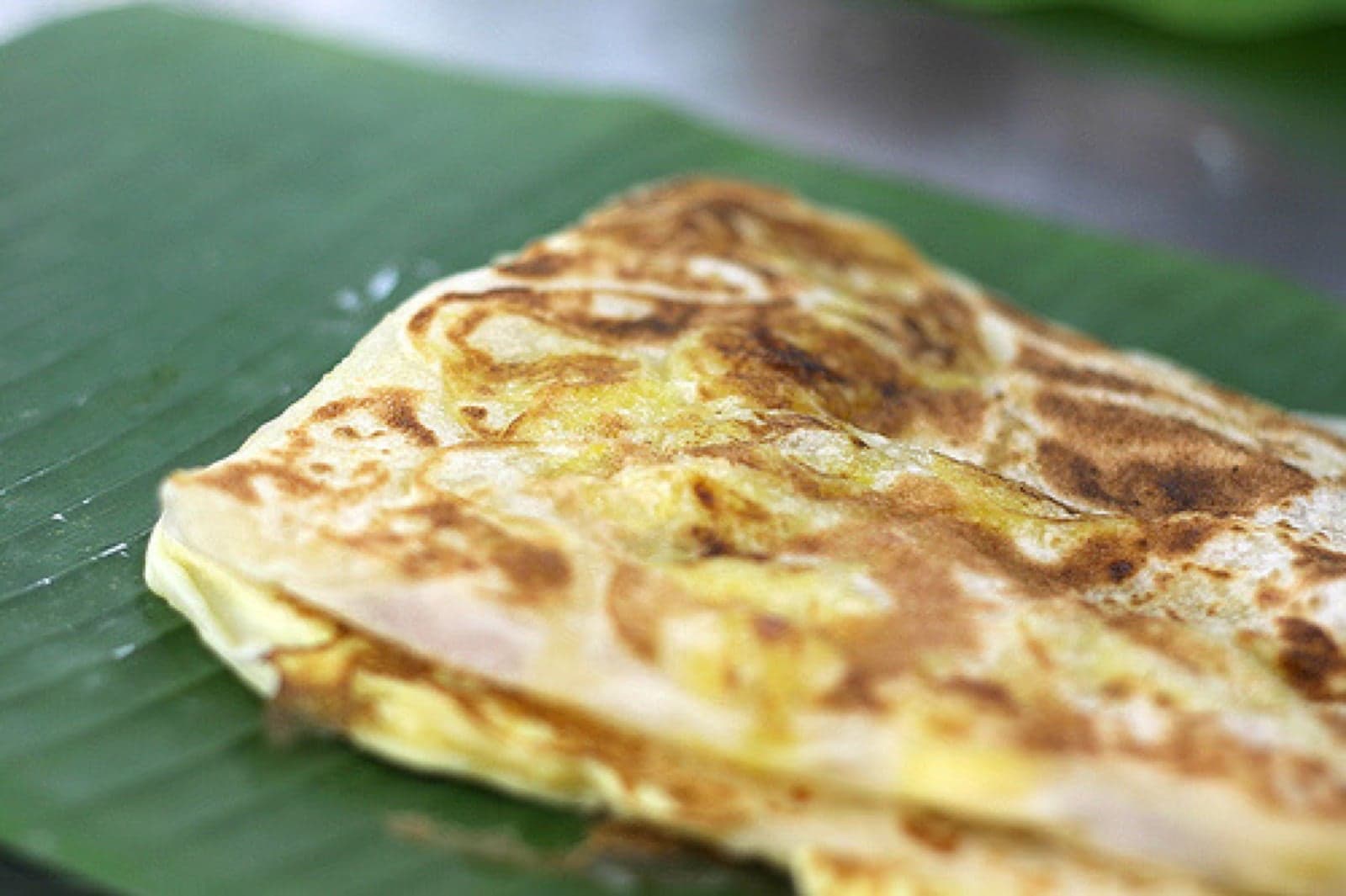 A flaky golden roti canai on a plate next to a small bowl of curry dipping sauce