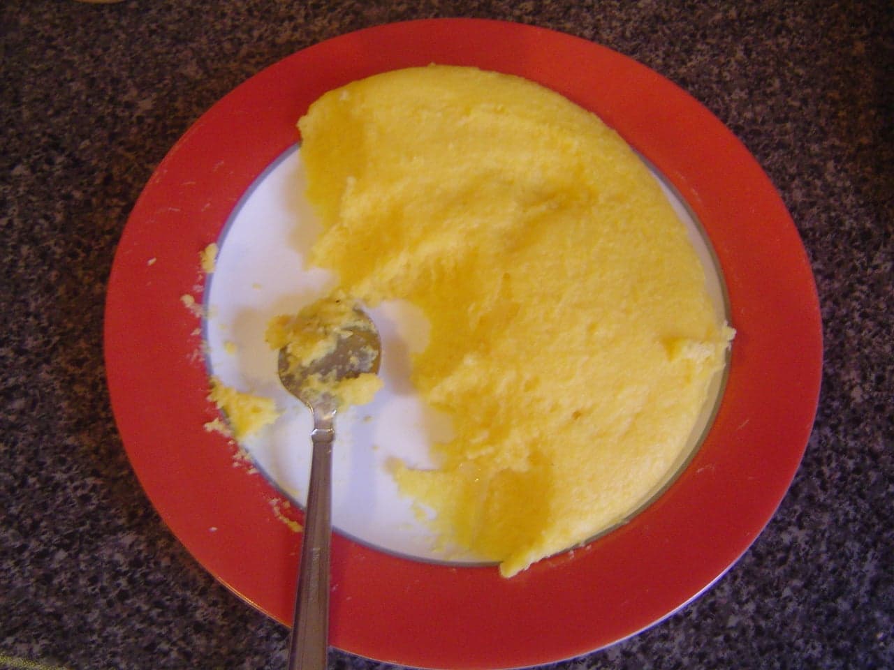 A golden dome of mămăligă corn porridge on a wooden board with sour cream beside it