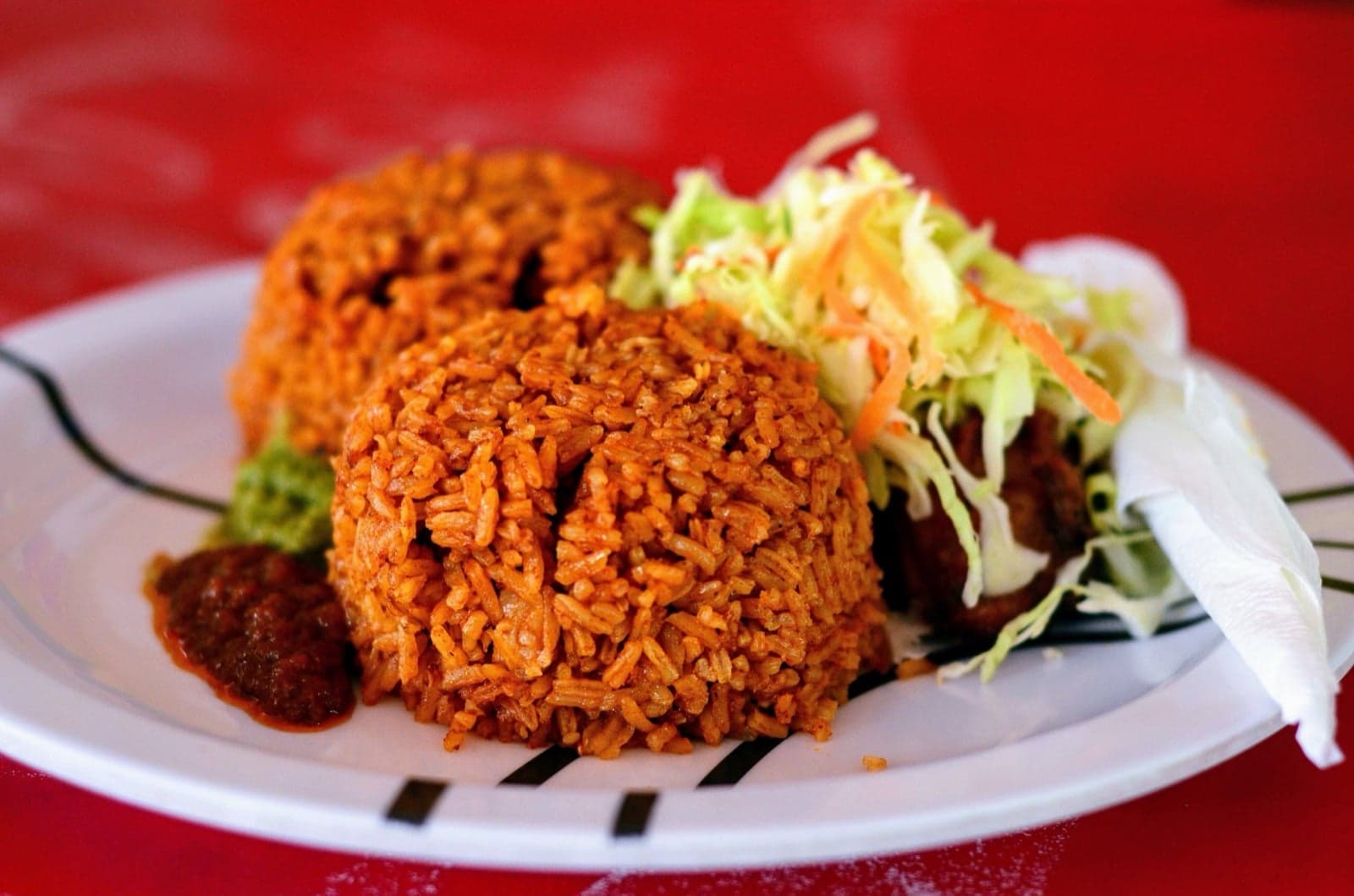A plate of Nigerian jollof rice with salad and a side dish