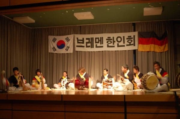 Four musicians in colourful Korean costumes playing large drums and gongs