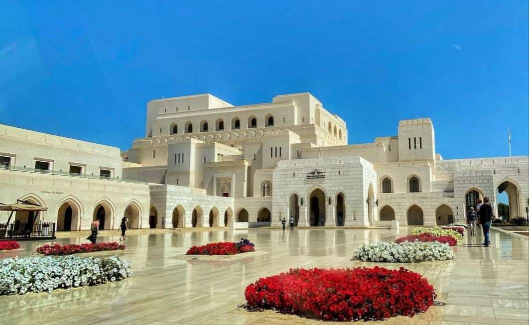 The Royal Opera House Muscat at night, lit up in warm light with its domed towers