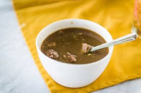 A bowl of rich brown goat water stew with bread on the side