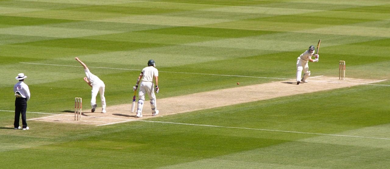 A cricket match being played on a green pitch in Saint Lucia with the sea visible in the background