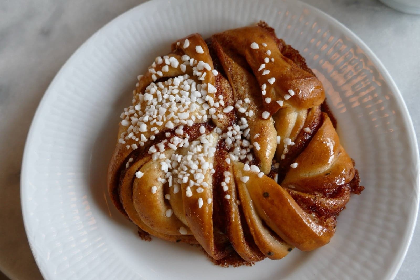 A classic Swedish cinnamon bun (kanelbulle) topped with pearl sugar