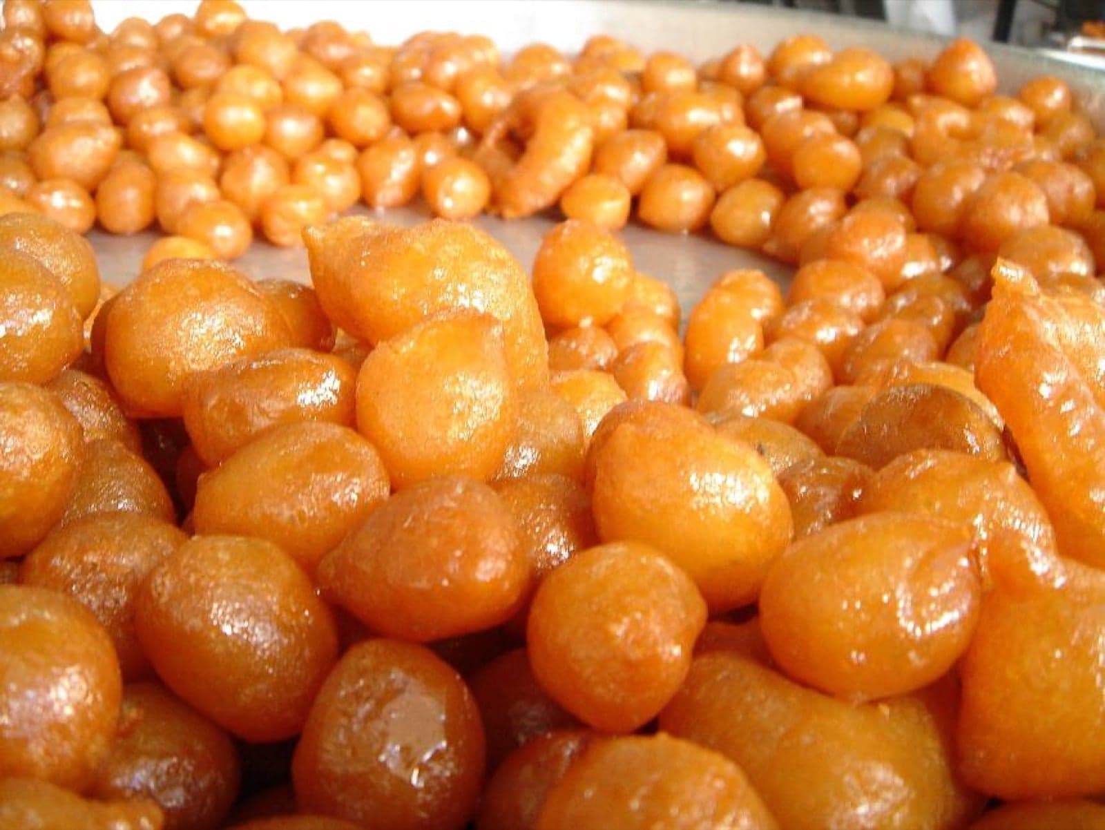 A plate of golden luqaimat dumplings drizzled with date syrup