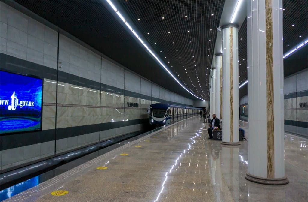 A grand, brightly lit station in the Tashkent metro with painted ceilings and decorated columns