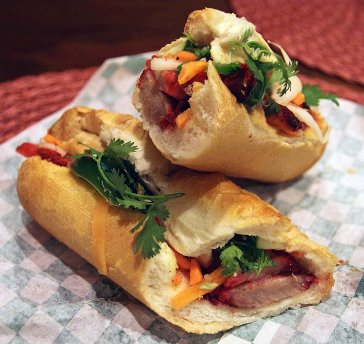 Two halves of a Vietnamese banh mi sandwich with grilled pork, fresh coriander, pickled carrots and chilli inside a crusty baguette