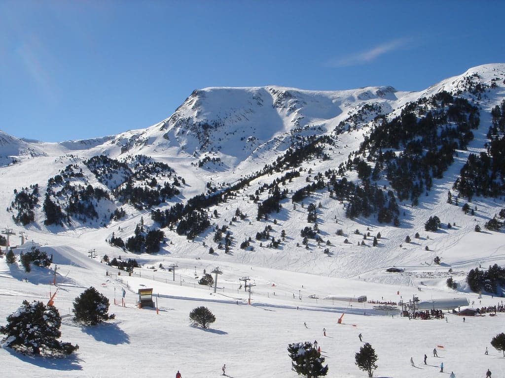 Skiers on a wide snowy slope with mountain panorama behind them in Andorra