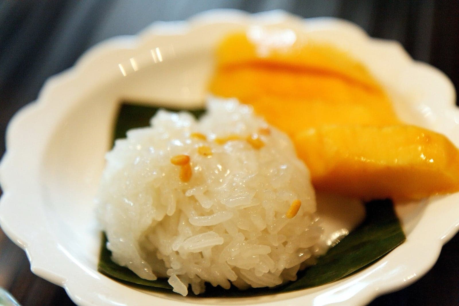 A bowl of warm sticky rice next to sliced ripe mango with sesame seeds
