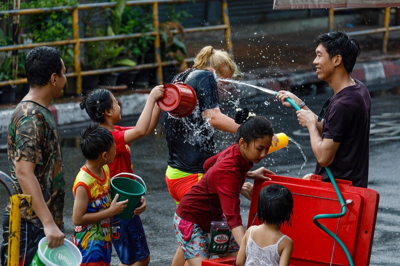Children and adults laughing as they splash each other with water buckets and hoses at Songkran